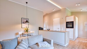 A modern living room with a sofa, a dining table, and a kitchen area with a built-in oven. - Newly built, modern, exclusive - that describes the Klein Stresow vacation village (Klein Stresow)