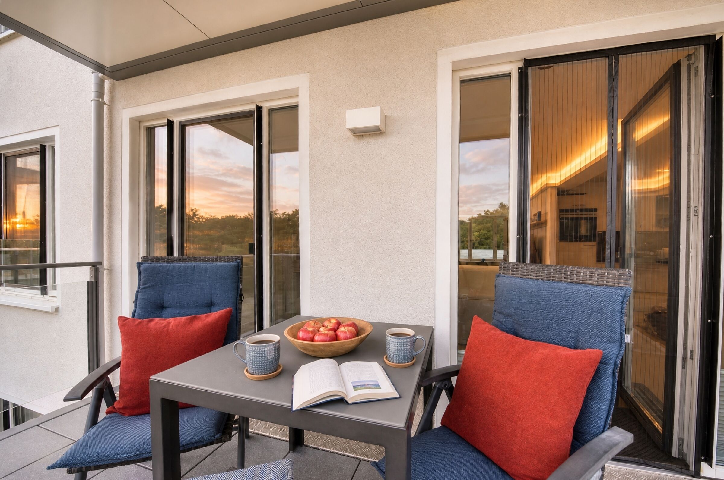 A balcony with two chairs, a table, a bowl of fruit, and two cups.