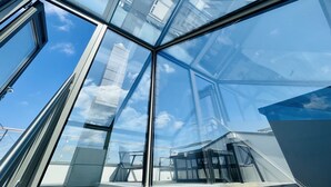 Een moderne glazen constructie met een helder uitzicht op de lucht en omliggende gebouwen.