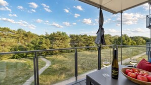 Een balkon met uitzicht op een bebost gebied, een fles wijn en een schaal appels.