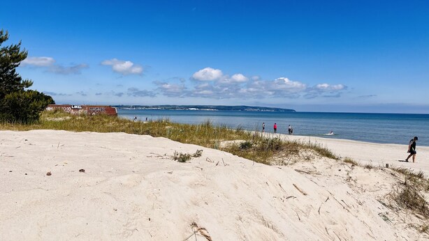 Een strand met duinen, een heldere blauwe lucht en een vergezicht op de kustlijn.