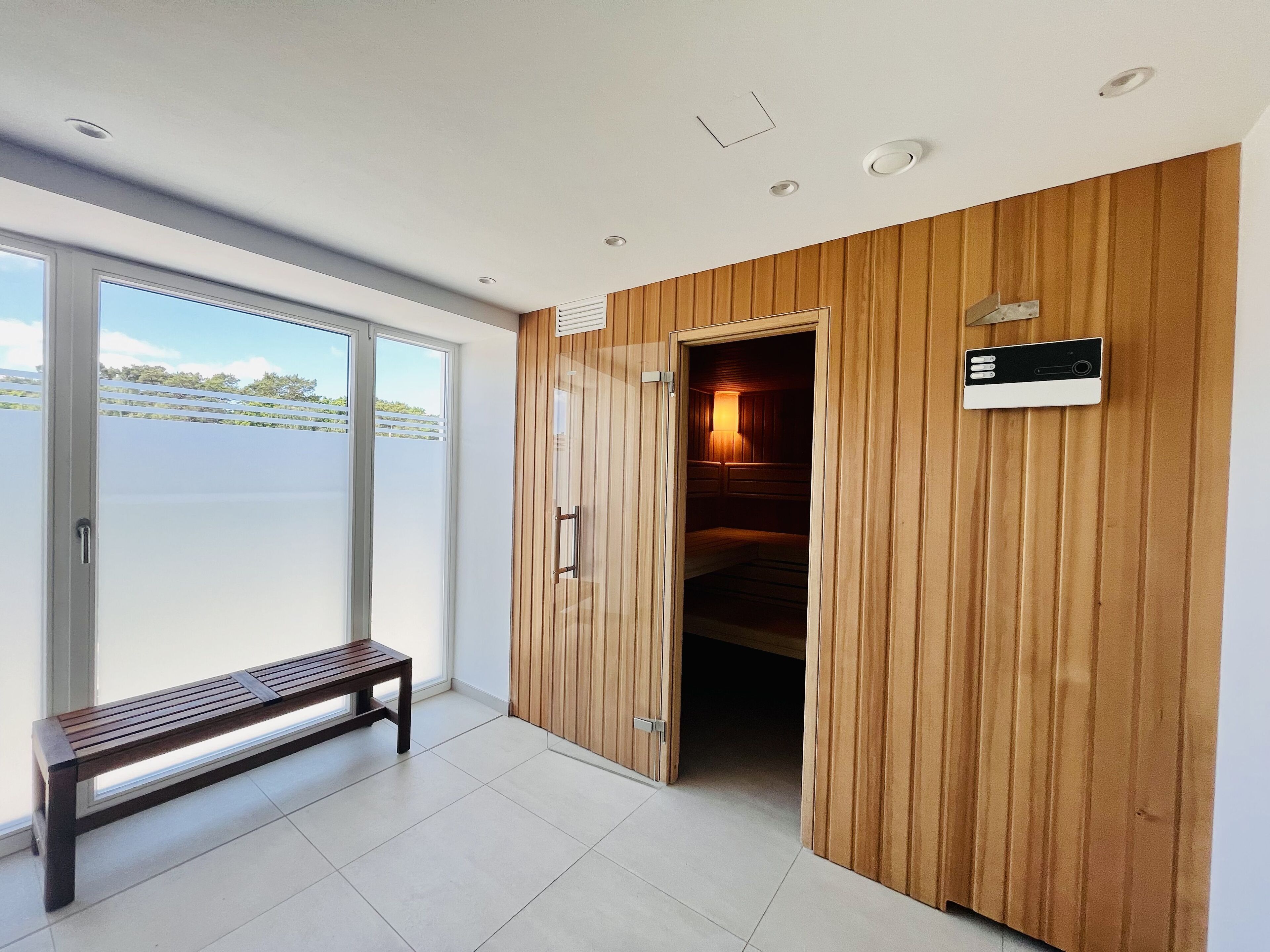 A modern interior with a bench, wooden panel walls, and a view through a glass door.