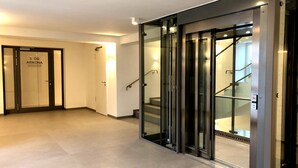 Een moderne hotel lobby met een glazen lift, een trap en een deur met de tekst '3. OG ARKONA'.