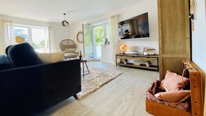 Una sala de estar moderna con un sofá, una silla de mimbre, una mesa de centro de madera, un globo terráqueo y un televisor en la pared.