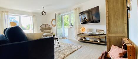 A modern living room with a sofa, a wicker chair, a wooden coffee table, a globe, and a TV on the wall.