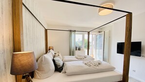 Una cama con dosel y estructura de madera, una mesita de noche con lámpara y un televisor de pantalla plana montado en la pared.