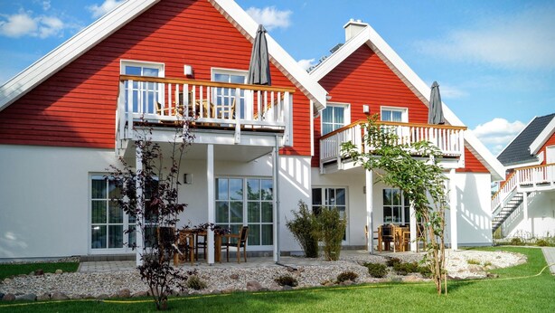 Una moderna casa a due piani con facciata rossa, decorazioni bianche e un balcone.