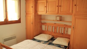 Un lit en bois avec une tête de lit, une fenêtre avec des rideaux et des armoires en bois intégrées au-dessus du lit.