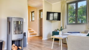 A living room with a fireplace, a flat-screen TV, a sofa, and a window with a view of trees. - Newly built, modern, exclusive - that describes the Klein Stresow vacation village (Klein Stresow)