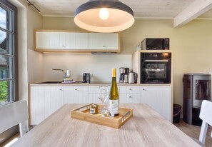 A modern kitchen with white cabinets, a wooden dining table with a wine bottle, glasses, and a jar. - Newly built, modern, exclusive - that describes the Klein Stresow vacation village (Klein Stresow)
