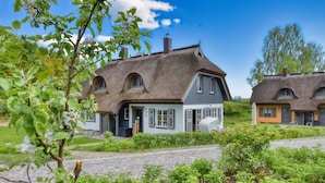 A traditional house with a thatched roof, a garden with a cobblestone path, and a clear blue sky. - Newly built, modern, exclusive - that describes the Klein Stresow vacation village (Klein Stresow)
