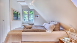 A bedroom with a large bed, a window, a bedside table with books, and a ceiling with skylights. - Newly built, modern, exclusive - that describes the Klein Stresow vacation village (Klein Stresow)
