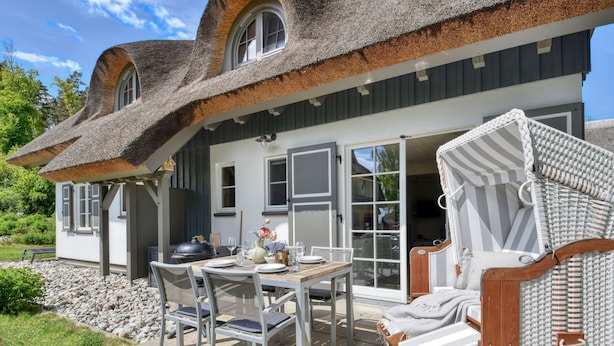A house with a unique curved roof, a patio with a table and chairs, and a wicker chair. - Newly built, modern, exclusive - that describes the Klein Stresow vacation village (Klein Stresow)