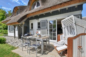 Et hus med et unikt buet tag, en terrasse med bord og stole, samt en fletstol.