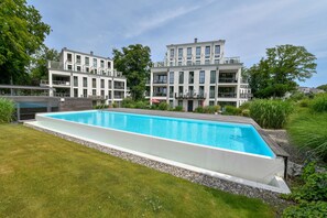 Ein modernes Hotel mit rechteckigem Pool, mehreren Balkonen und üppiger Bepflanzung.