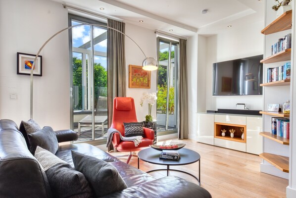 Ein modernes Wohnzimmer mit einer Ledersofa, einem roten Sessel, einem runden Couchtisch und einem großen Fernseher.
