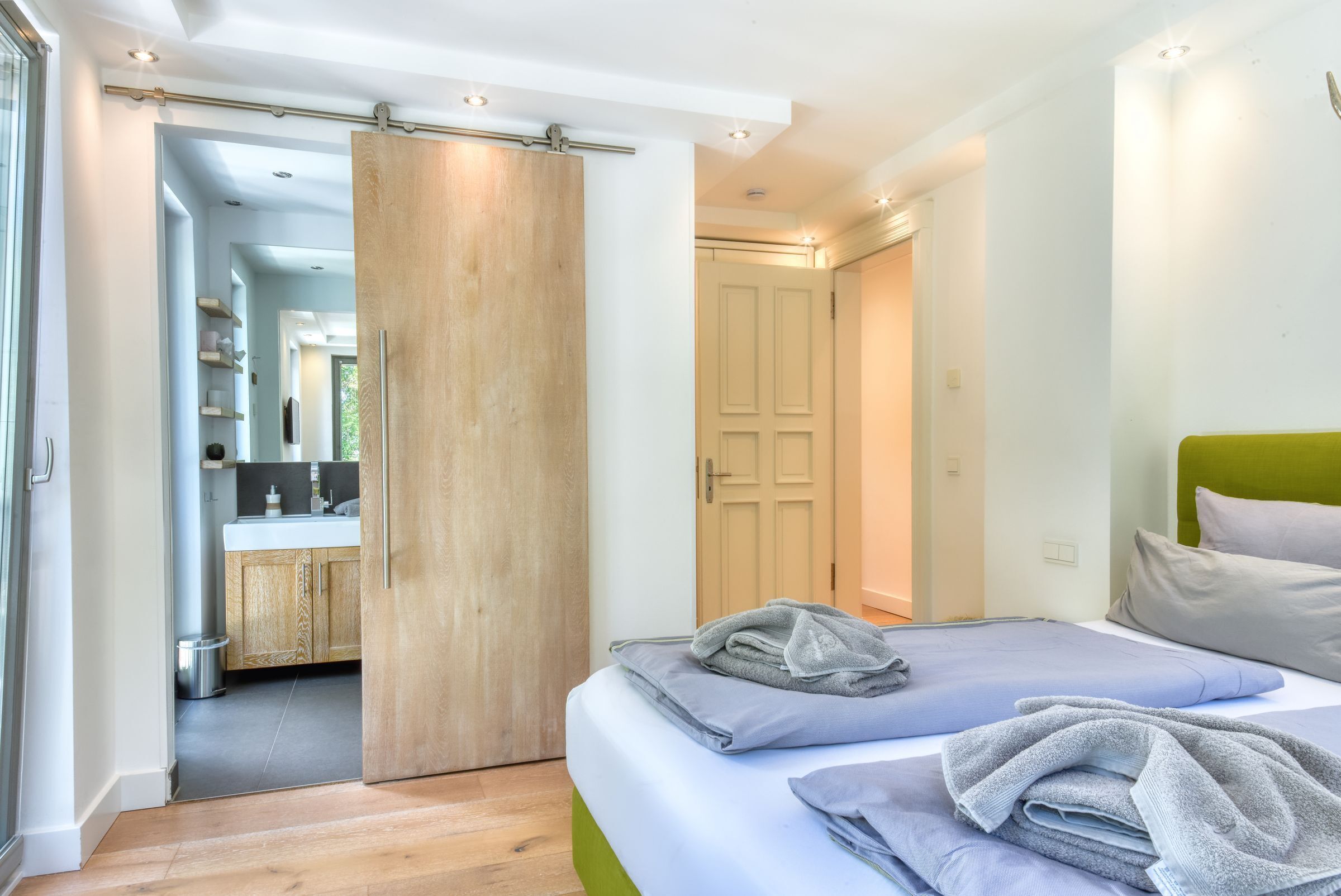 Een moderne slaapkamer met een groot bed, een groen hoofdeinde en een badkamer door een geopende deur zichtbaar.