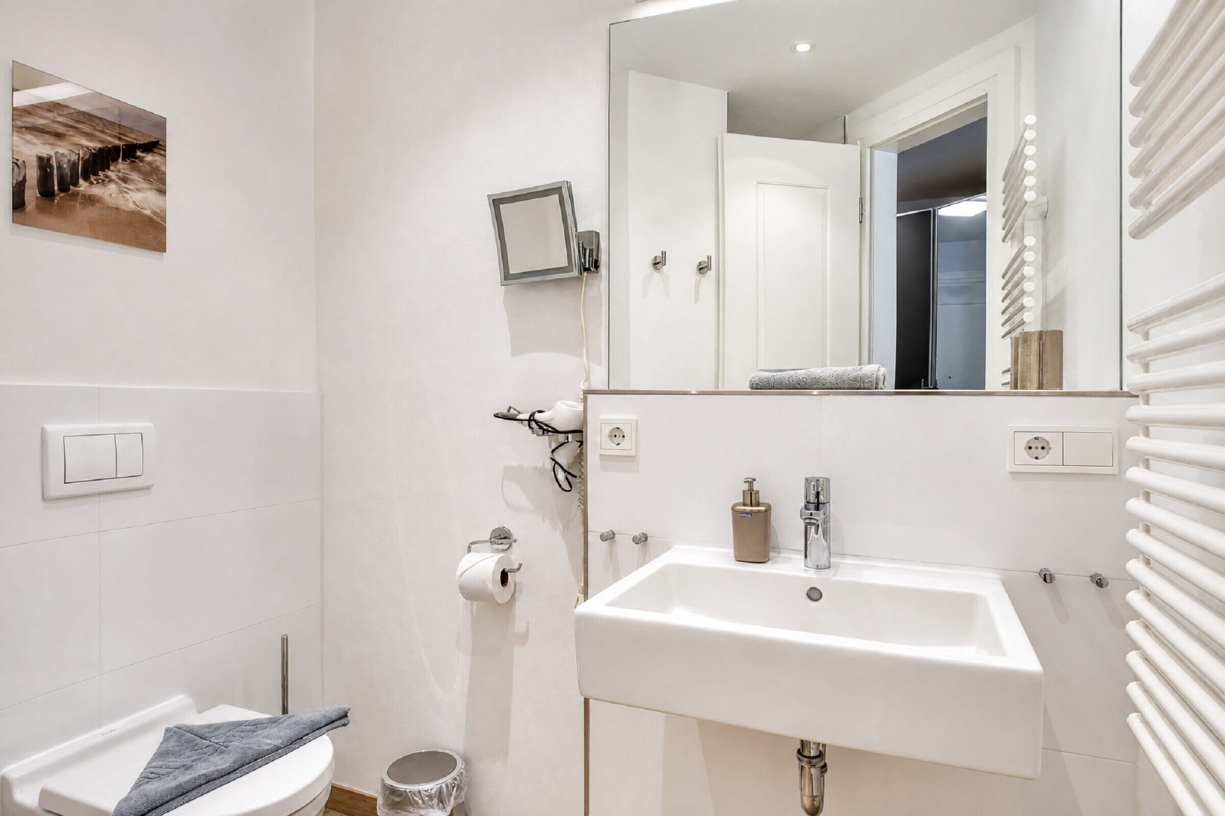 Ein modernes Badezimmer mit einem weißen Waschbecken, Spiegel und einer Toilette.