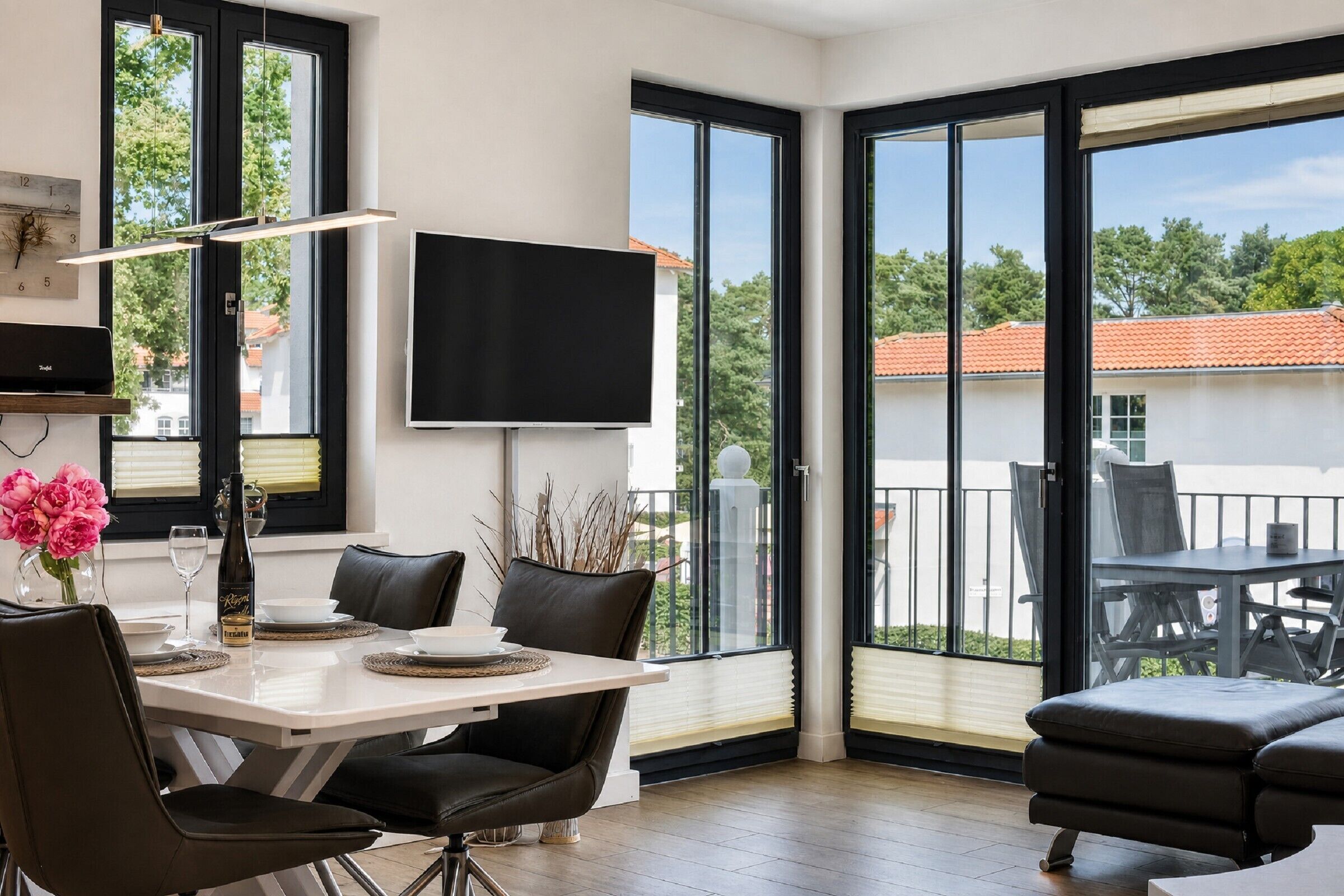 Een moderne woonkamer met een eethoek, grote ramen en een flatscreen televisie.