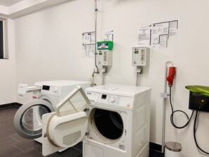 A laundry room with two front-loading washing machines, a green detergent dispenser, and a red fire extinguisher. - Light-flooded vacation apartment 'Lachmöwe' in Baabe: sea view, comfort (Baabe)