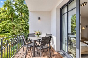 A balcony with a table and chairs, a vase of flowers, and a view of greenery and a building.