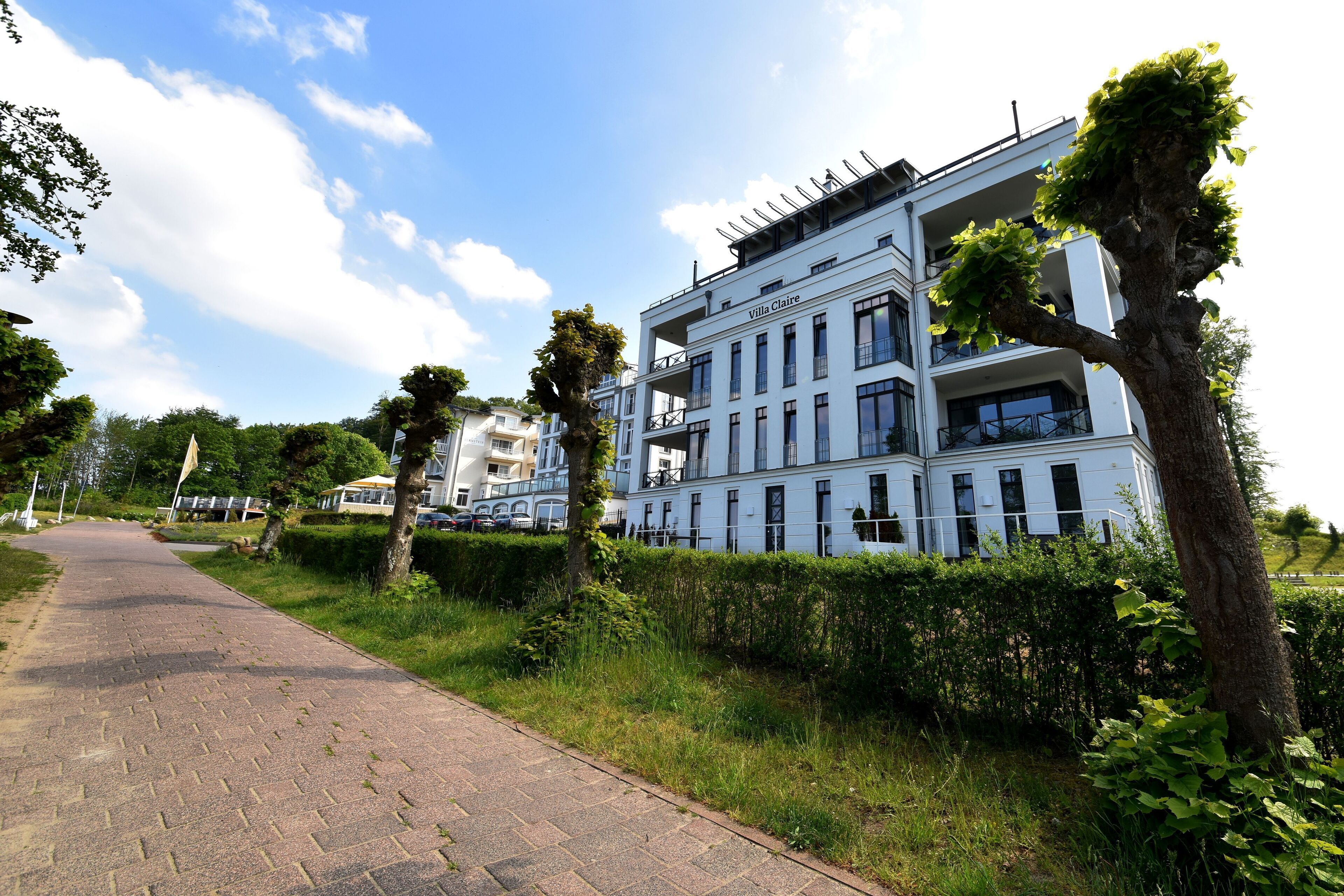 A modern building with the name "Villa Claire" on the facade, surrounded by greenery and a paved walkway.