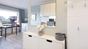 Une cuisine moderne avec des meubles blancs, une grande fenêtre et un coin repas comprenant une table et des chaises.