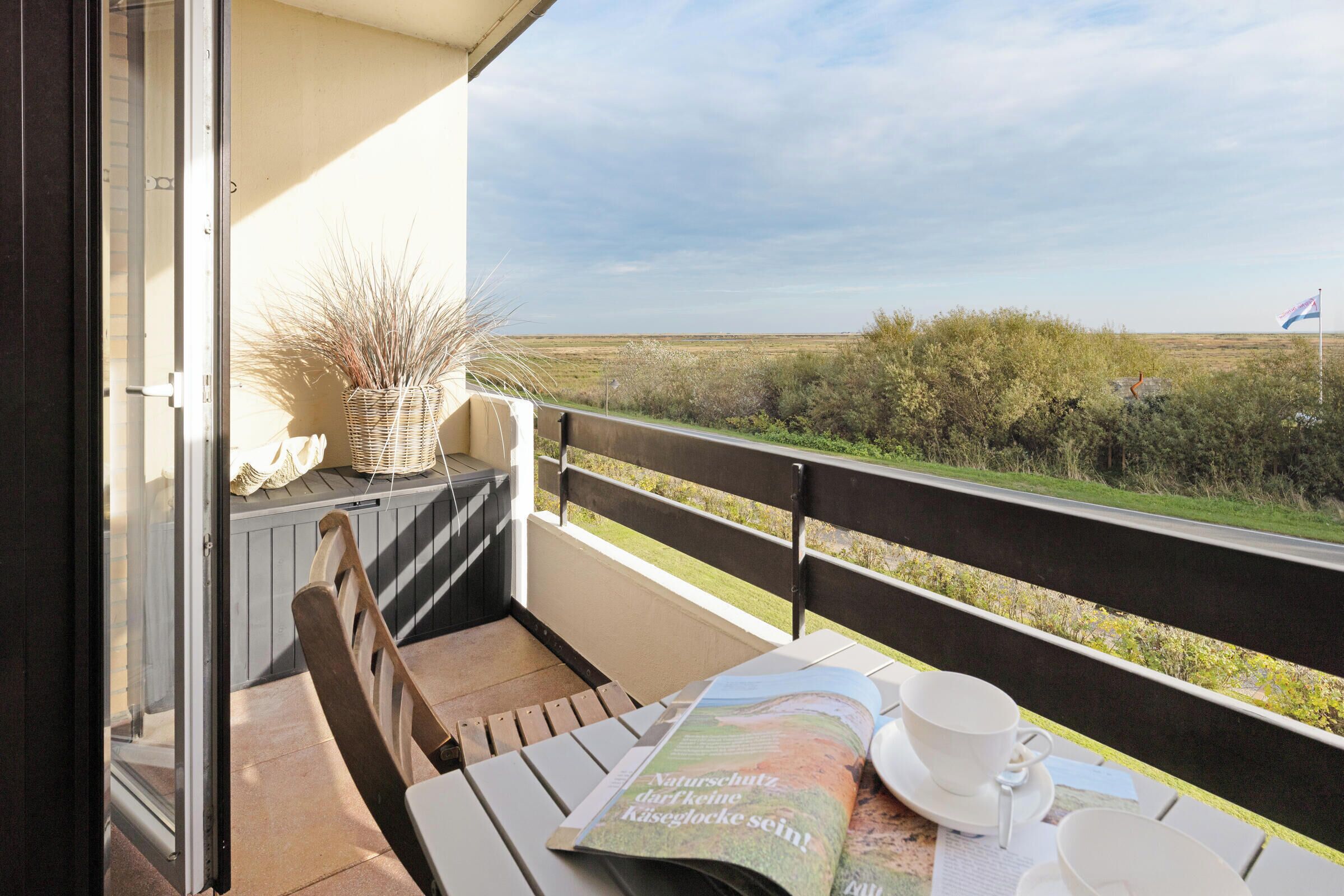 A balcony with a view of the countryside, a table with a magazine, a cup, and a saucer.