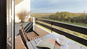 Un balcon donnant sur la campagne, une table avec un magazine, une tasse et une soucoupe.