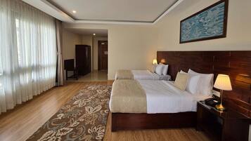 Habitación de hotel con dos camas, cabecera de madera, mesita de noche con lámpara, ventana grande con cortinas traslúcidas y un cuadro en la pared.