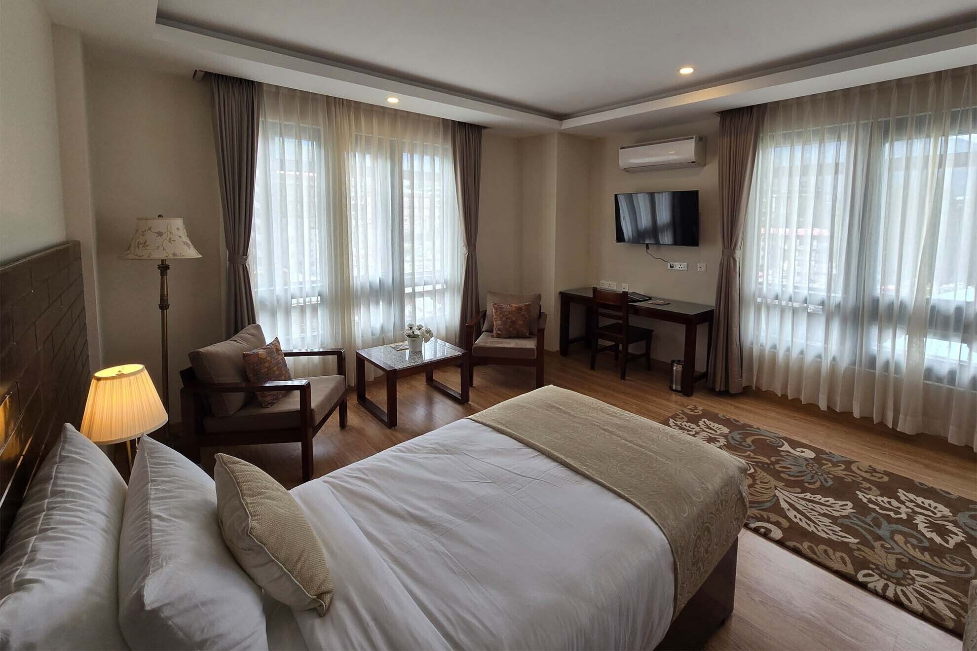 Una habitación de hotel con una cama grande, un escritorio, una silla, una lámpara y un televisor.