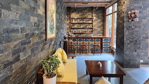Un rincón de bar acogedor con paredes de piedra, estantes de madera y una zona de estar con mesa y sillas.