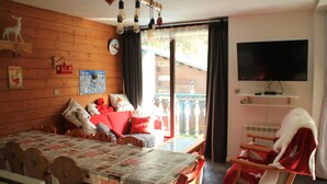A cozy room with a wooden wall, a bed with a quilt, a red chair, a television, and a balcony with a view. - Moulin Ml161 Telecabine & Nature 6 Pers (Chatel)