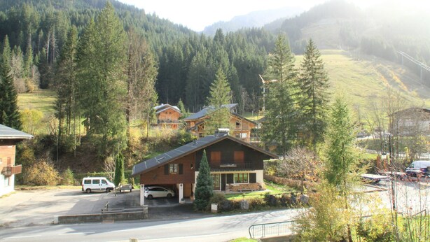 A mountain lodge with a large wooden structure, a driveway, and a parking area with vehicles. - Moulin Ml161 Telecabine & Nature 6 Pers (Chatel)