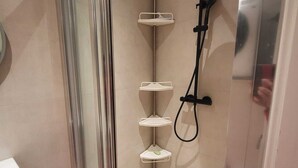 Un espace douche doté d’une porte en verre, d’un pommeau de douche à main et de plusieurs étagères pour les articles de toilette.