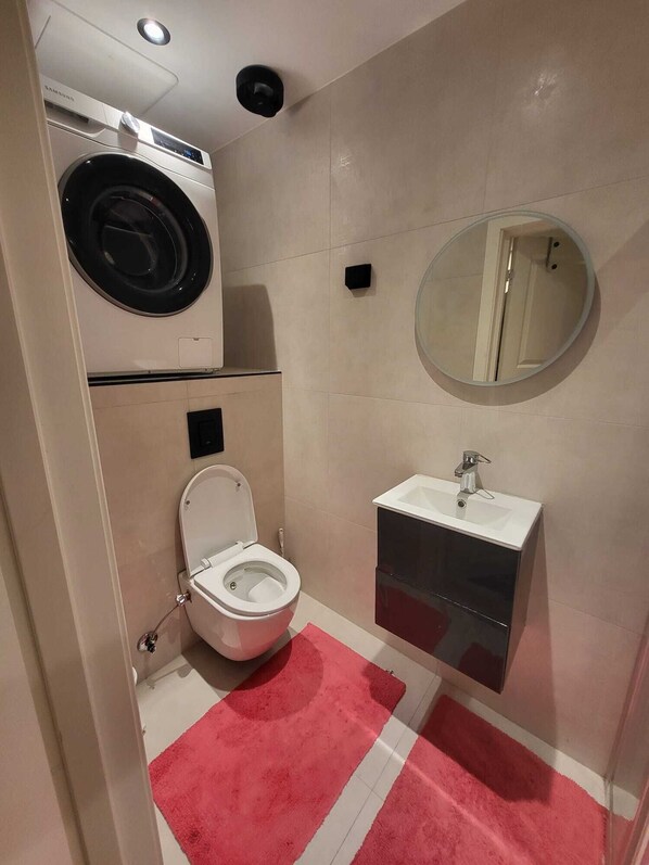 Un baño pequeño con lavadora, inodoro, lavabo y espejo.