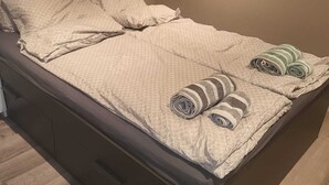 Un lit simple avec une couette beige, deux oreillers et deux serviettes enroulées.