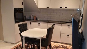 Une cuisine moderne avec des meubles blancs, un four noir et un coin repas comprenant une table blanche et deux chaises.