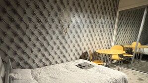 Ein modernes Schlafzimmer mit einem gepolsterten Kopfteil, einem Bett mit weißer Daunendecke und einem kleinen Tisch mit Stühlen.