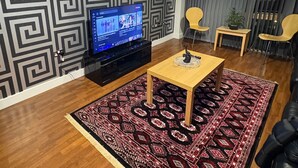 Ein Wohnzimmer mit Wandmuster, einem Flachbildfernseher, einem Holztisch, einem Teppich mit Muster und einer Ledersofa.