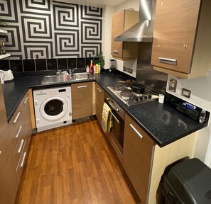 A compact kitchen with a built-in washer, a stove, and a sink. - Jupiter Building 2 Bedroom Apartment Birmingham (Birmingham)
