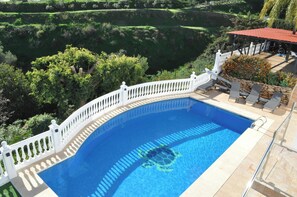 A swimming pool with a white fence, surrounded by lush greenery and a red-roofed structure.