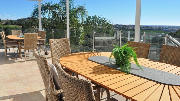 Um pátio externo com móveis de vime, uma mesa redonda e um vaso de planta.