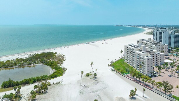 A coastal hotel with a beach view, a parking area, and a small lake.
