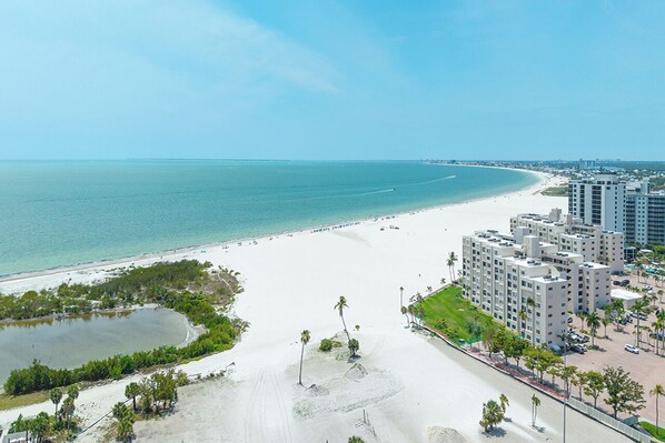A coastal hotel with a beach view, a parking area, and a small lake.