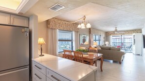 A modern kitchen with a built-in island, dining area with wooden furniture, and a living room with a sofa and a balcony.