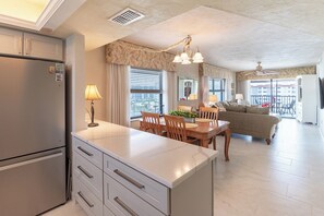 A modern kitchen with a built-in island, dining area with wooden furniture, and a living room with a sofa and a balcony.