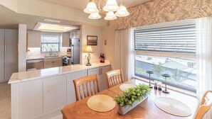 A modern kitchen with a central island, a dining area with a wooden table, and a view through large windows.