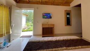 Een slaapkamer met een houten plafond, een bed, een televisie op een standaard en een deur die uitkomt op een tuin.