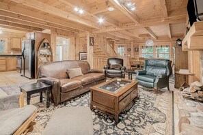 A wooden interior with a leather sofa, two armchairs, a coffee table, and a fireplace.